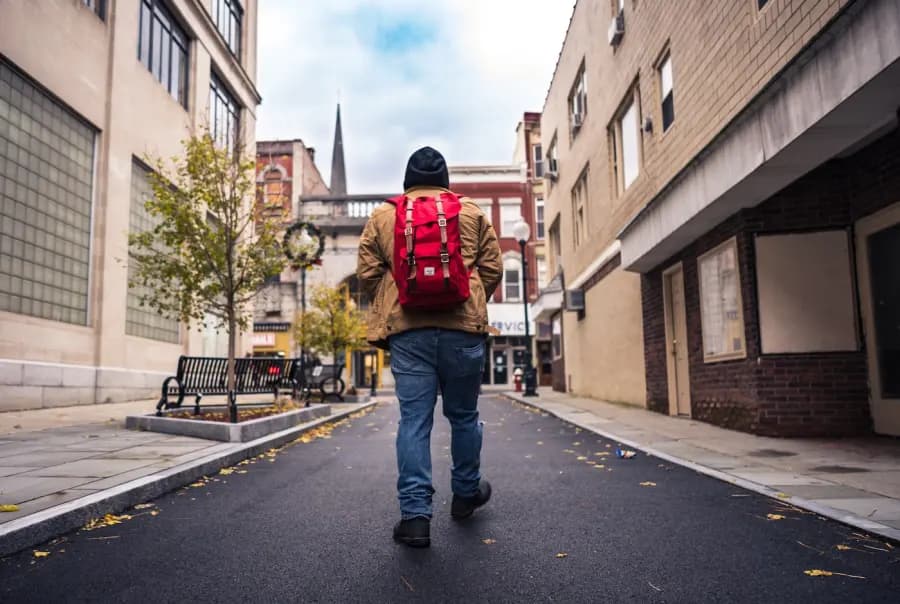A person walking through a city street with a bright red backpack