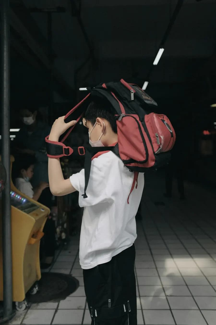 A person holding a red backpack over one shoulder in a transit station