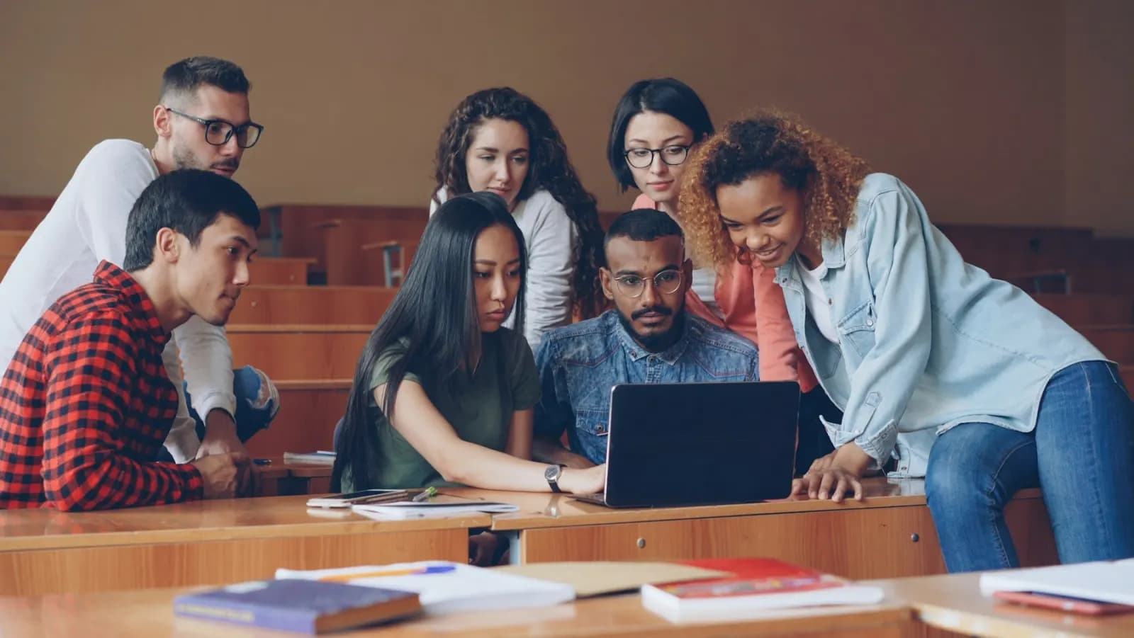 Students collaborating around a laptop in a lecture hall
